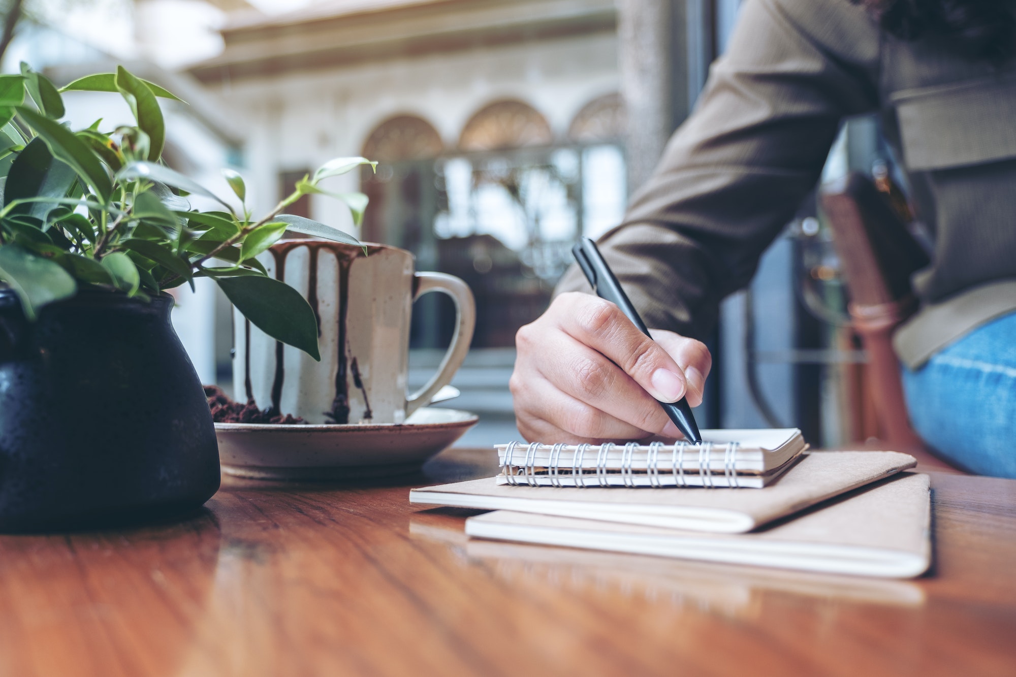 Closeup image of a woman's hand writing on blank notebook with coffee cup on wooden table